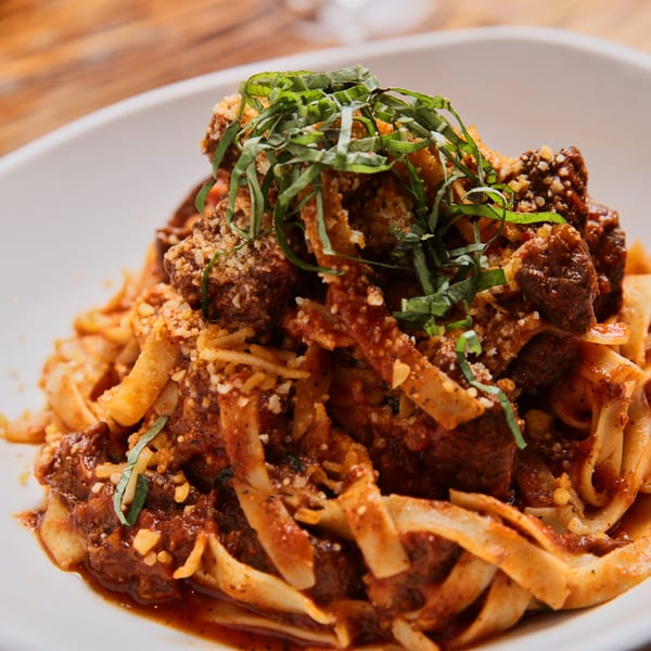 Close-up of tagliatelle pasta with meatballs, red sauce, parmesan, and fresh basil on a white plate.