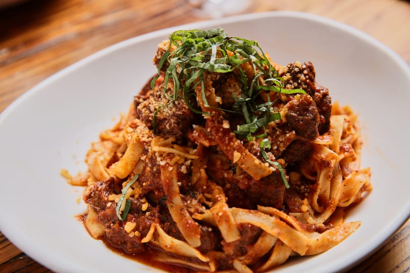 Close-up of tagliatelle pasta with meatballs, red sauce, parmesan, and fresh basil on a white plate.