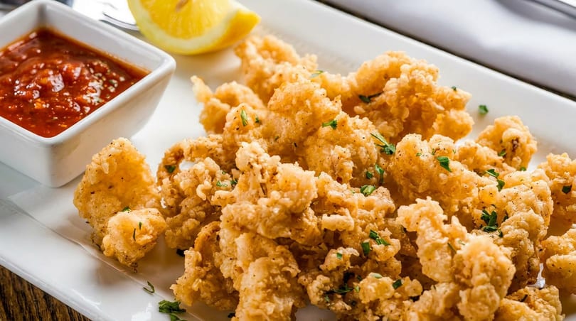 Golden fried calamari with marinara sauce, a lemon wedge, and parsley on a white plate.