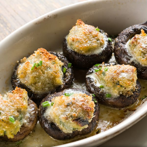 Six baked stuffed mushrooms with golden-brown tops and chives in a white oval dish.