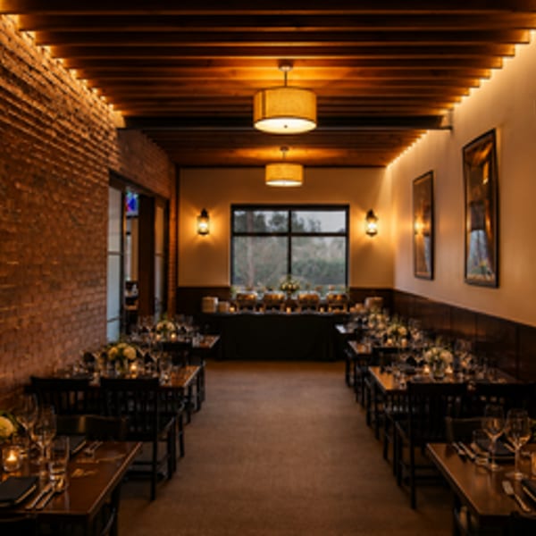 Warmly lit restaurant dining room with set tables, brick wall, and a buffet in the background.