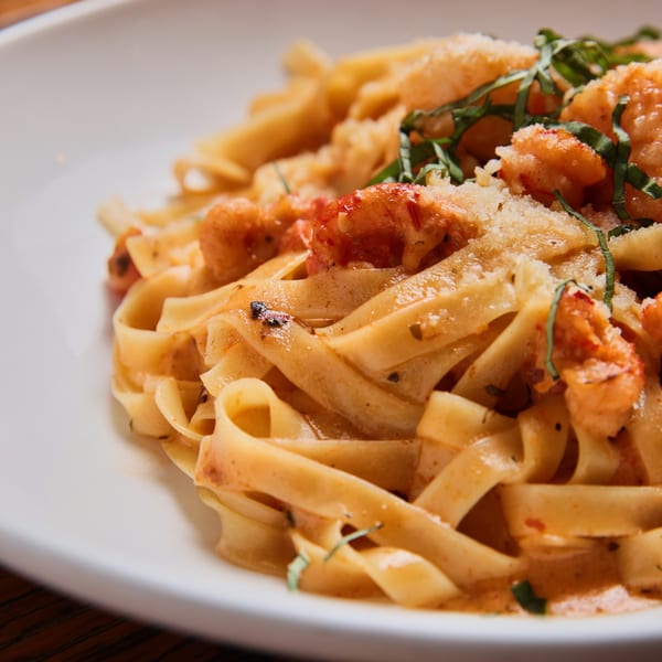 Close-up of fettuccine pasta with shrimp, red sauce, parmesan cheese, and basil on a white plate.