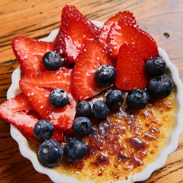 Crème brûlée topped with fresh sliced strawberries and blueberries in a white ramekin.