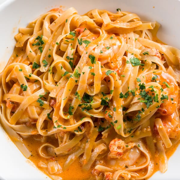 Fettuccine pasta with shrimp and a creamy tomato sauce, garnished with fresh parsley in a white bowl.