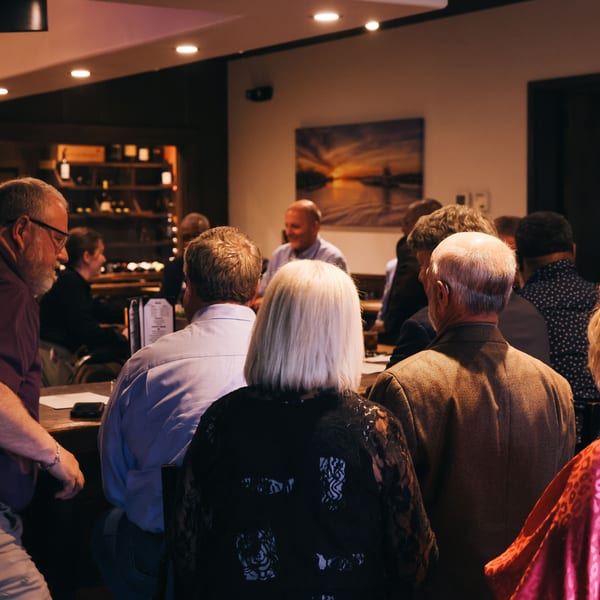 Patrons gathered at a dimly lit bar, some seated, others standing, enjoying the evening.