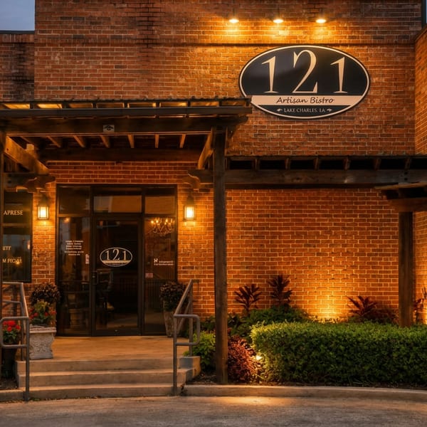 The illuminated brick exterior of 121 Artisan Bistro with an inviting entrance and landscaping at dusk.