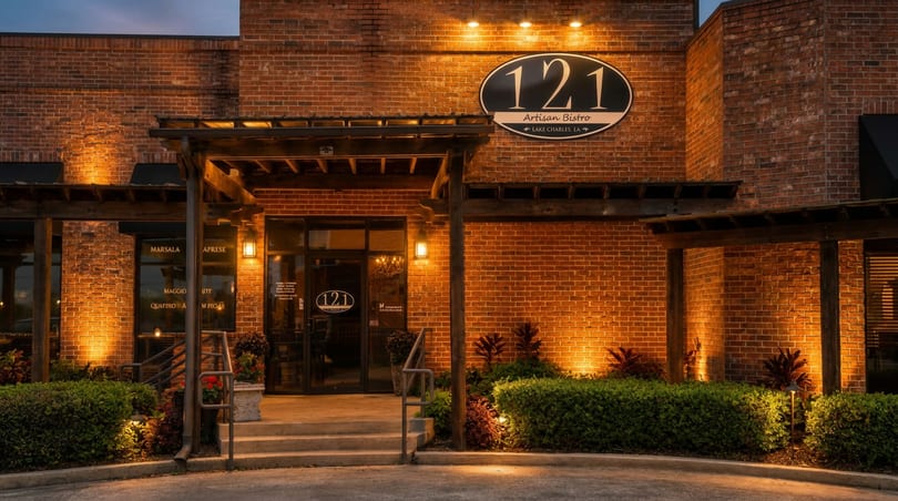 Illuminated brick exterior of 121 Artisan Bistro at dusk, with a welcoming entrance and landscaping.