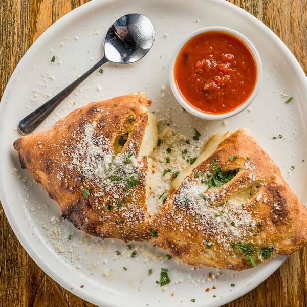 Golden-brown calzone halves with melted cheese, parmesan, and parsley, served with a side of marinara.