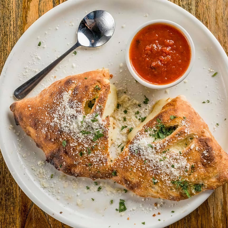 Golden-brown calzone halves with melted cheese, parmesan, and parsley, served with a side of marinara.