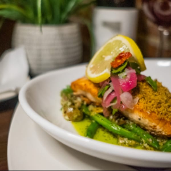 Pan-seared salmon with green beans, pesto, pickled onions, and a lemon slice on a white plate.