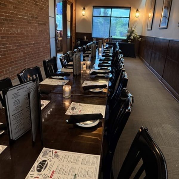 Long dining table set for a private event, with menus, plates, and candles, in a rustic room.