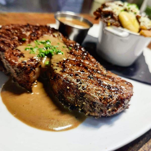 Grilled steak with sauce and chives, served with a side of fries in a white ramekin.