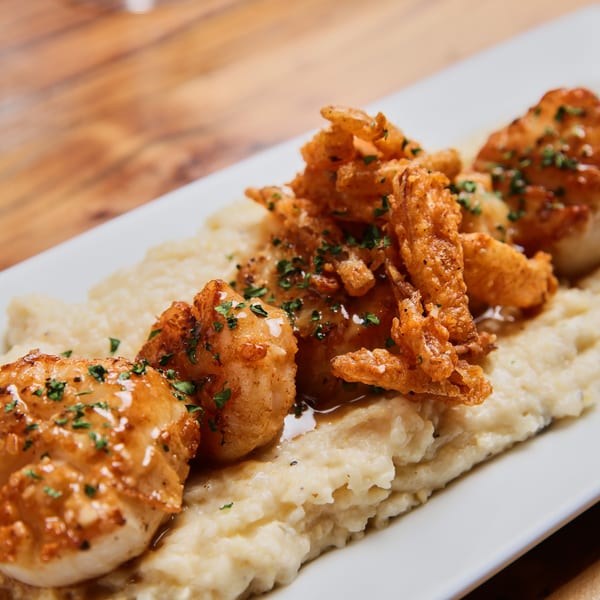 Crispy fried seafood and shrimp with gravy and herbs served over creamy mashed potatoes on a white platter.