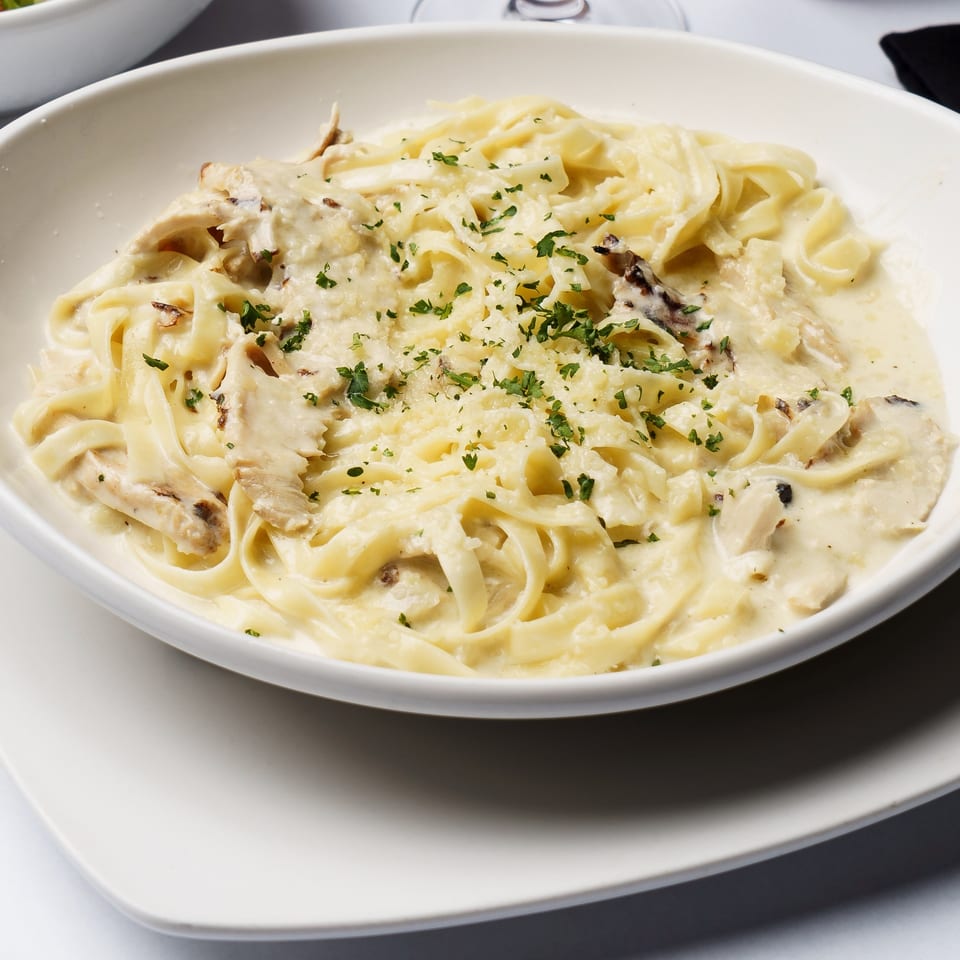 Creamy chicken fettuccine Alfredo topped with Parmesan and parsley, served in a white bowl on a restaurant table.