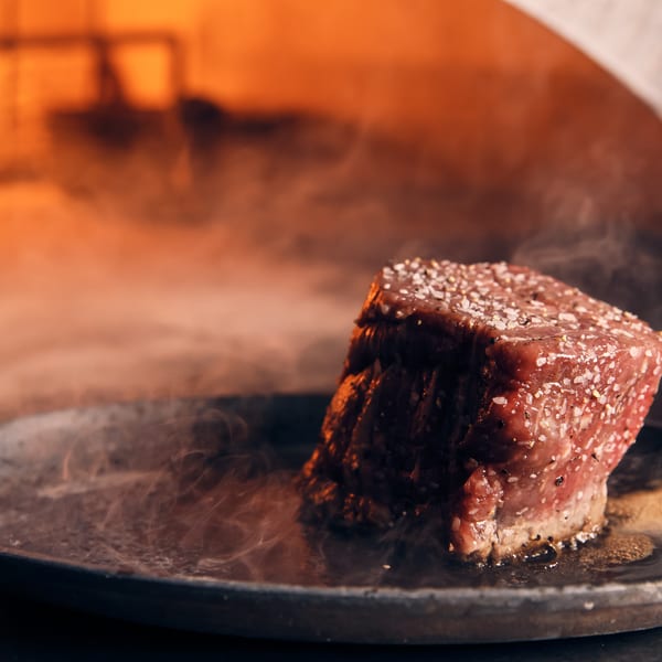 Thick cut steak seasoned with salt and pepper sizzling on a hot plate with smoke rising.