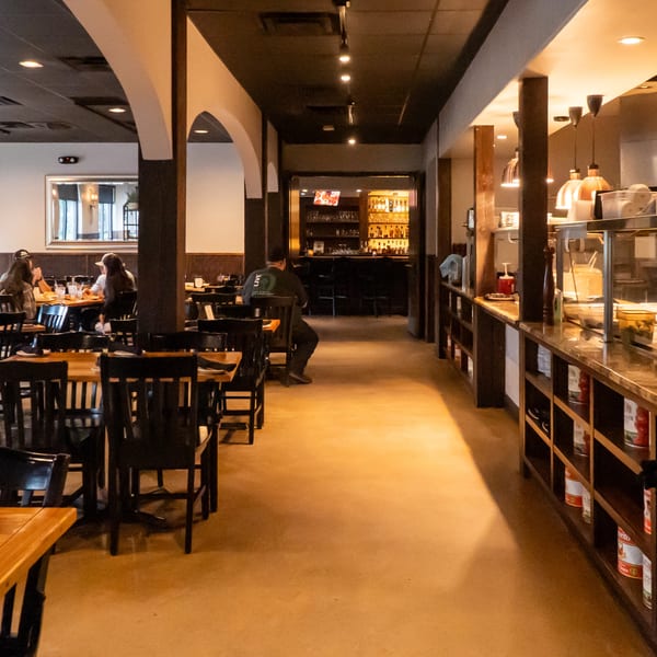 A restaurant interior with dining tables, a bar area, and an open kitchen pass-through.