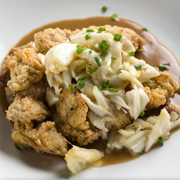 Fried oysters topped with crab meat, chives, and a brown sauce on a white plate.