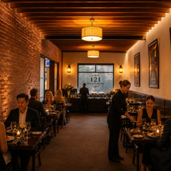 Diners enjoying meals in a warmly lit restaurant with exposed brick and a visible "121 Artisan Bistro" sign.