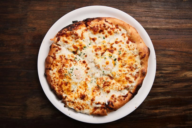 A whole pizza with melted cheese, baked eggs, and green herbs on a white plate.