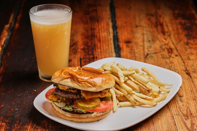 Double cheeseburger with fries and a glass of beer on a rustic wooden table.