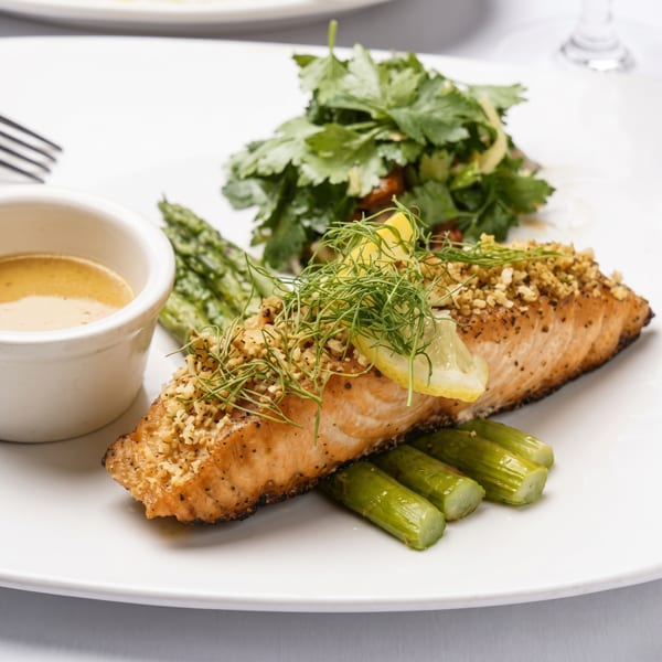 Seared fish fillet topped with herbs and crumbs, served with grilled vegetables, greens, lemon, and dipping sauce.