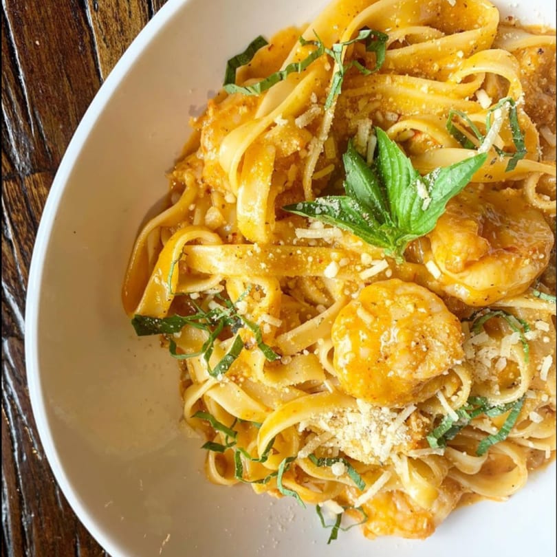 Fettuccine pasta with shrimp, creamy orange sauce, parmesan cheese, and fresh basil in a white bowl.