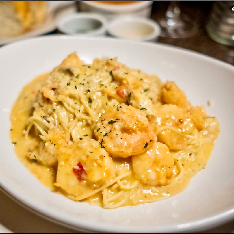 Shrimp scampi pasta with creamy sauce and parsley in a white bowl.