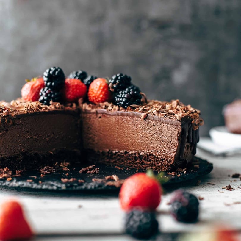 Decadent chocolate cheesecake with a slice removed, topped with fresh strawberries and blackberries.