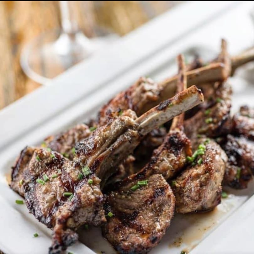 Grilled lamb chops with visible char marks and chives, served on a white rectangular platter.
