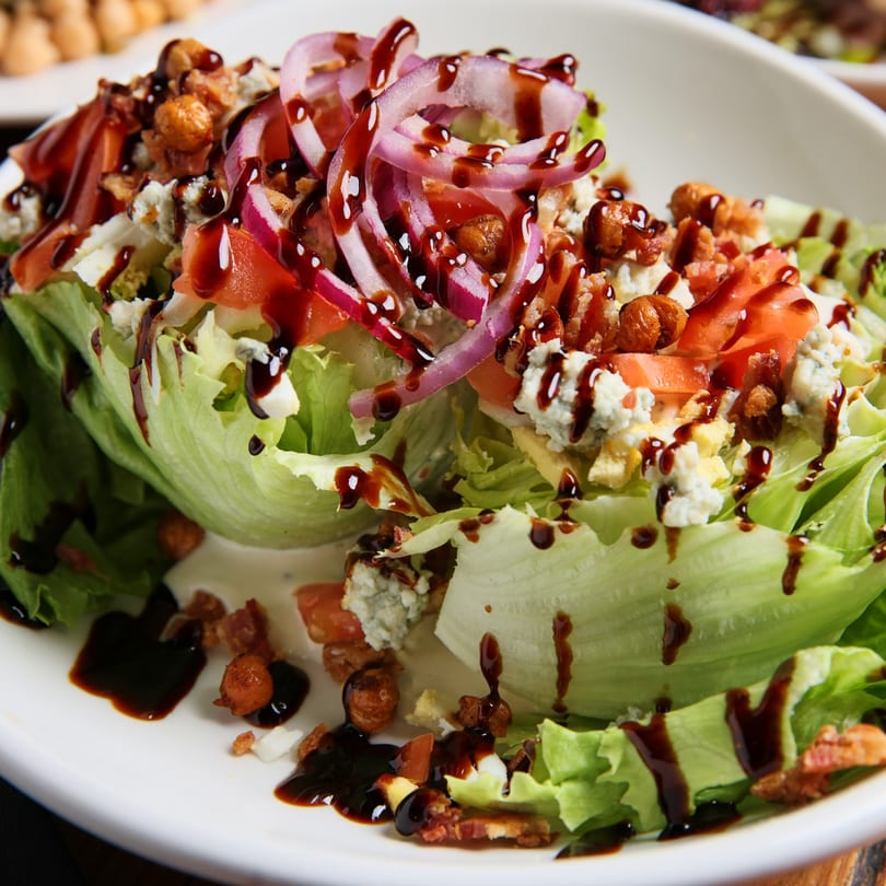 A fresh wedge salad with red onions, tomatoes, bacon, blue cheese, and balsamic glaze.