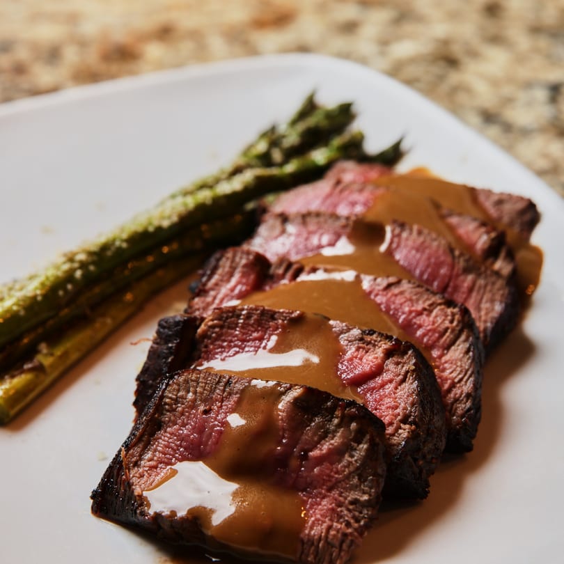 Sliced steak with gravy and a side of asparagus on a white plate.