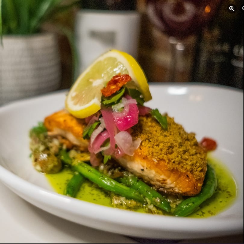 Crispy salmon with green beans, pickled onions, and a lemon slice on a white plate.